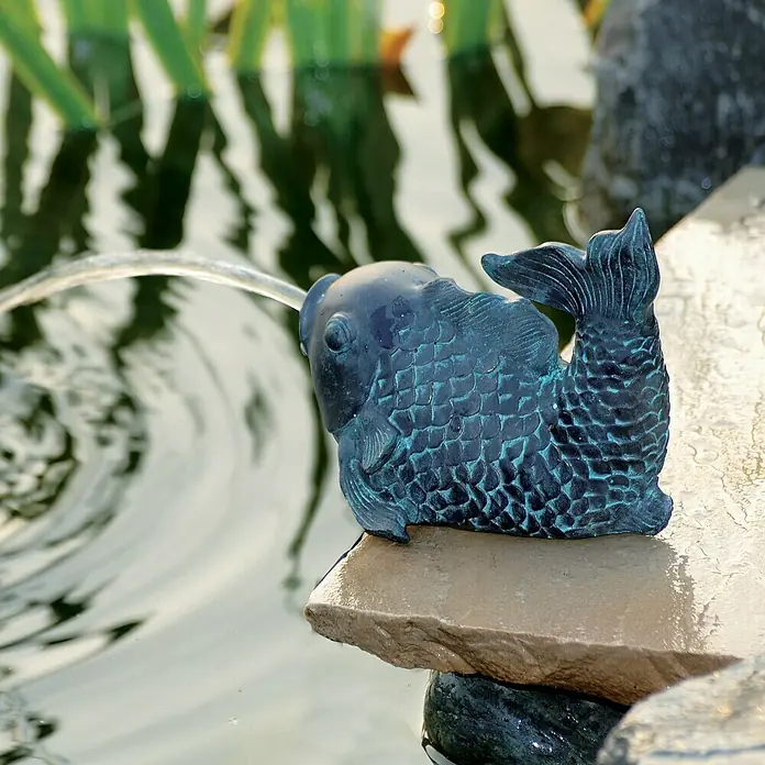 Ubbink Teichpumpe Pond Decor 900 L/H - Geeignet für: Wasserspeier, 16 W - Nahaufnahme einer blauen Fischbrunnenfigur, aus der Wasser in einen Teich fließt, der Gartenbrunnen verleiht dem Außenbereich einen Hauch von Ruhe.