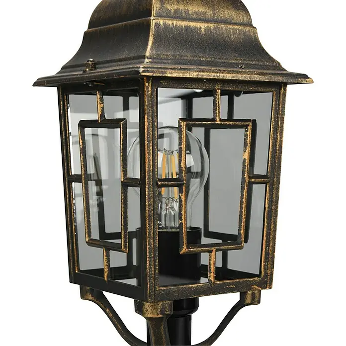 Trio Lighting Sobremuro exterior Volturno - Color del marco: Bronce, 17 x 15 x 47 cm, Sin bombillas - Primer plano de una lámpara de exterior decorativa de bronce con un cerramiento de vidrio transparente y una bombilla Edison en su interior.