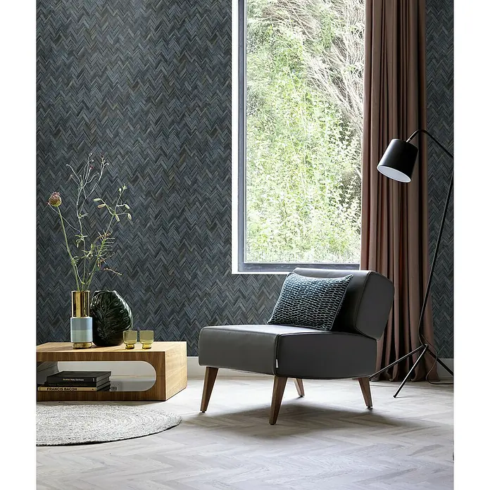 Rasch Beachhouse Vliestapete Vintage Fischgrätmuster - Dunkelblau, Holzoptik, 10,05 x 0,53 m - Elegantes graues Ledersessel mit Zierkissen und Holzbeinen vor gemusterter Tapete, neben einem Couchtisch mit Dekoration und einer Stehlampe.