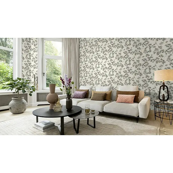 Rasch Selection Vliestapete Vinyl Botanical - Schwarzbraun, Floral, 10,05 x 0,53 m - Helles Wohnzimmer mit einem modernen Sofa, das mit verschiedenen Kissen dekoriert ist, und einem dekorativen Beistelltisch mit einer Lampe.