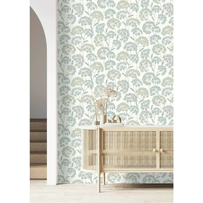 Rasch Selection Vliestapete Vinyl Blümchen - Pastelltürkis, Floral, 10,05 x 0,53 m - Eine Nahaufnahme einer Wand mit einer floralen Tapete in Blau- und Grüntönen, die ein Sideboard mit Rattandetails hervorhebt.