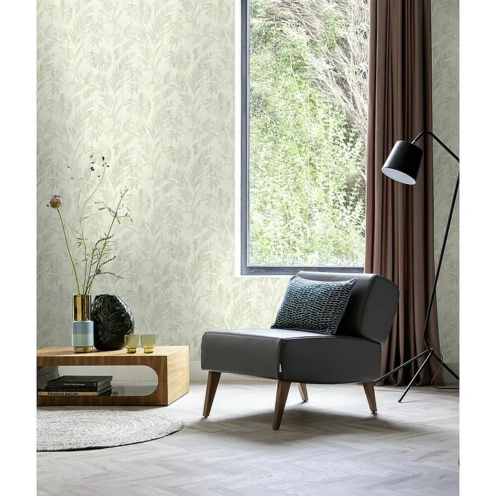 Rasch Beachhouse Vliestapete Pastelles Pflanzenmotiv - Hellgrün, Floral, 10,05 x 0,53 m - Ein grauer Sessel mit einem blauen Kissen steht in einem modernen Wohnzimmer mit tropischer Tapete und einer Stehlampe.