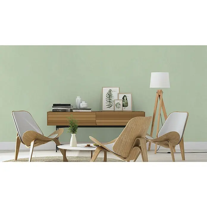 Rasch Vliestapete Deco Style - Grün, Uni, 10,05 x 0,53 m - Helle Inneneinrichtung mit zwei Schichtholzstühlen und einer passenden Kommode, dekoriert mit grünen Pflanzen und Kunstwerken.