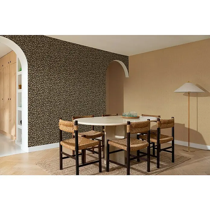 Rasch Amara Vliestapete - Kupferschwarz, Grafisch, 10,05 x 0,53 m - Ein Esszimmer mit einem ovalen Tisch, umgeben von Stühlen mit Rattanlehnen und einem auffälligen gemusterten Wanddesign.
