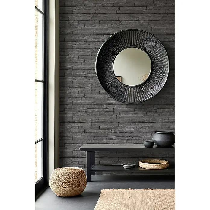 Rasch Selection Vliestapete Vinyl - Anthrazit, Steinoptik, 10,05 x 0,53 m - Einrichtungsidee mit einem runden Spiegel an einer dunklen Ziegelwand, ergänzt durch einen schwarzen Tisch, Körbe und einen Hocker für ein stilvolles Ambiente.