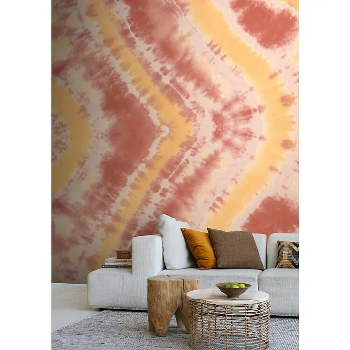 Rasch Beachhouse Fototapete Batikoptik I - B x H: 300 x 265 cm, Vlies, Rot - Dekoratives Wandbild mit abstraktem Batikmuster in Rot- und Gelbtönen über einem hellen Sofa mit Kissen.