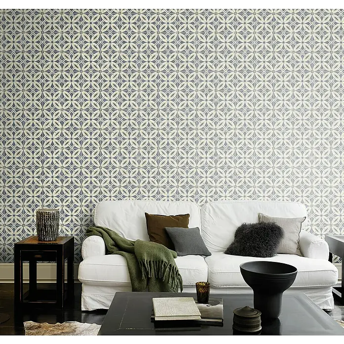 Rasch Beachhouse Vliestapete Fliesenkacheln - Dunkelblau/Beige, Fliesenoptik, 10,05 x 0,53 m - Elegantes Wohnzimmer mit weißem Sofa vor einer Wand mit geometrischem Muster. Dekorative Kissen und ein grüner Überwurf ergänzen das Interieur.