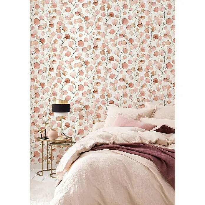 Rasch Selection Vliestapete Vinyl Blattzweige - Pastell-Rotbraun, Floral, 10,05 x 0,53 m - Schlafzimmer mit Bettwäsche in Rosatönen und einer Nachttischlampe auf einem goldfarbenen Tisch vor einer Wand mit floralem Muster.