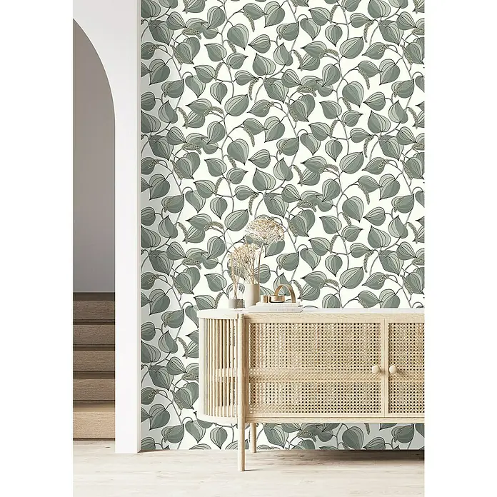 Rasch Selection Vliestapete Vinyl Botanical - Grün, Floral, 10,05 x 0,53 m - Nahaufnahme eines Raumes mit einer Kommode vor einer Wand mit Blättermuster-Tapete.