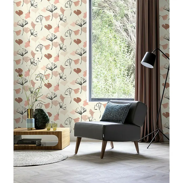 Rasch Selection Vliestapete Vinyl Modernes Blattmotiv - Weißbraun, Floral, 10,05 x 0,53 m - Graues Ledersessel mit blauem Kissen vor einem Fenster mit Blick auf üppiges Grün, ergänzt durch eine elegante Stehlampe und einen Holztisch.