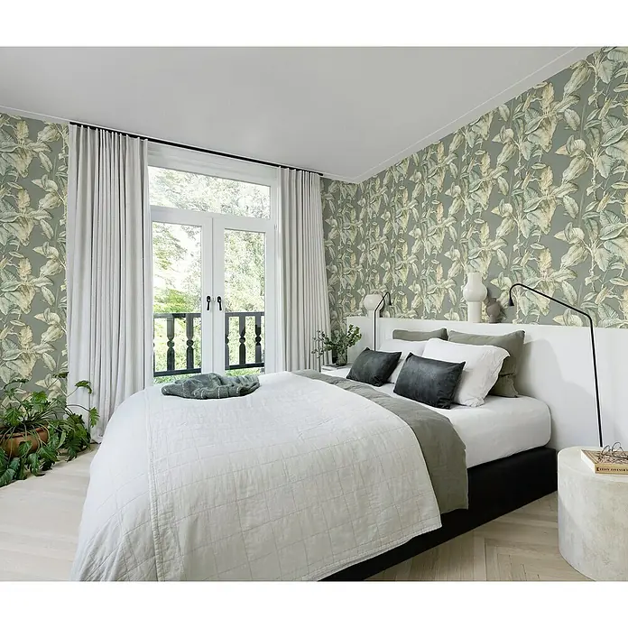 Rasch Back To Nature Vliestapete Blätter - Grun-Beige, Floral, 10,05 x 0,53 m - Einladendes Schlafzimmer mit einem großen Bett, geschmückt mit weicher Bettwäsche und Kissen, vor einer Wand mit auffälliger Blättertapete.