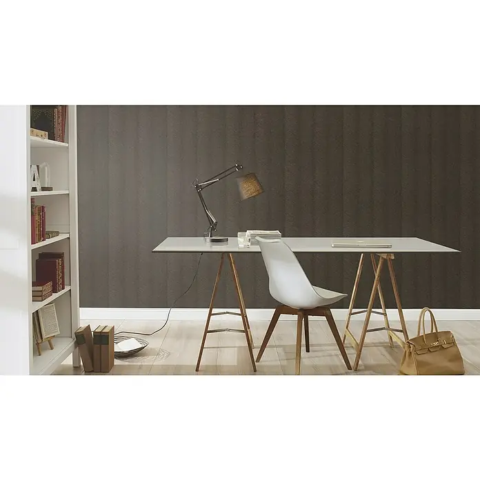 Rasch Amara Vliestapete - Schwarzbronze, Grafisch, 10,05 x 0,53 m - Ein Arbeitszimmer mit einem hellen Schreibtisch, einem modernen Stuhl, einer Lampe und einem Bücherregal. Die braune Handtasche rundet den Raum ab.