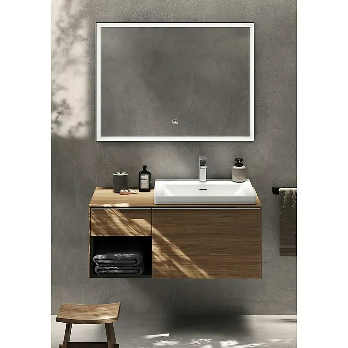 Villeroy & Boch Subway 3.0 Waschtisch - 67 x 55,2 cm, Mit schmutzabweisender Glasur, Hahnloch: Mitte, Mit Überlauf, Stone White, Geschliffen - Moderner Waschtisch aus Holz mit weißem Waschbecken und beleuchtetem Spiegel vor Betonwand. Dunkle Handtücher liegen darunter, daneben ein Holzschemel.