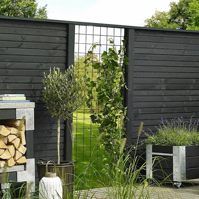 Plus Sichtschutzelement Plank - 174 x 166 cm, Schwarz (RAL 9005) - Eine idyllische Gartenszene mit einem eleganten schwarzen Holzzaun, der durch eine Metallgitterstruktur und üppige Vegetation ergänzt wird.