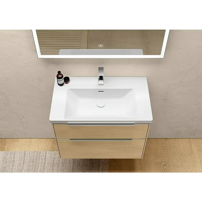 Villeroy & Boch Subway 3.0 Waschbeckenunterschrank - Nordik Oak, Anzahl Schubladen: 2 Stk., Farbe Griff: Aluminium glänzend, B x T x H: 77,2 x 47,8 x 57,6 cm - Ein moderner Waschtisch mit einer weißen Keramikspüle und einem Unterschrank aus hellem Holz, gekrönt von einem beleuchteten Spiegel.