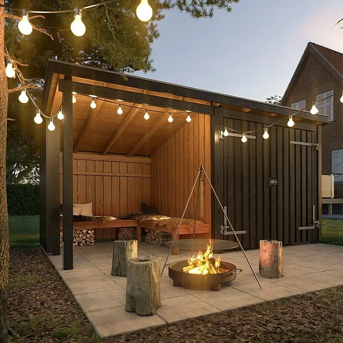Plus Gartenhaus Grillhütte - Außenmaß inkl. Dachüberstand (B x T): 446 x 237 cm, Holz, Halboffen - Ein einladender Außenbereich mit dunklem Holzunterstand, leuchtenden Lichterketten und einer zentralen Feuerstelle mit Holzsitzen auf einer gepflasterten Terrasse.