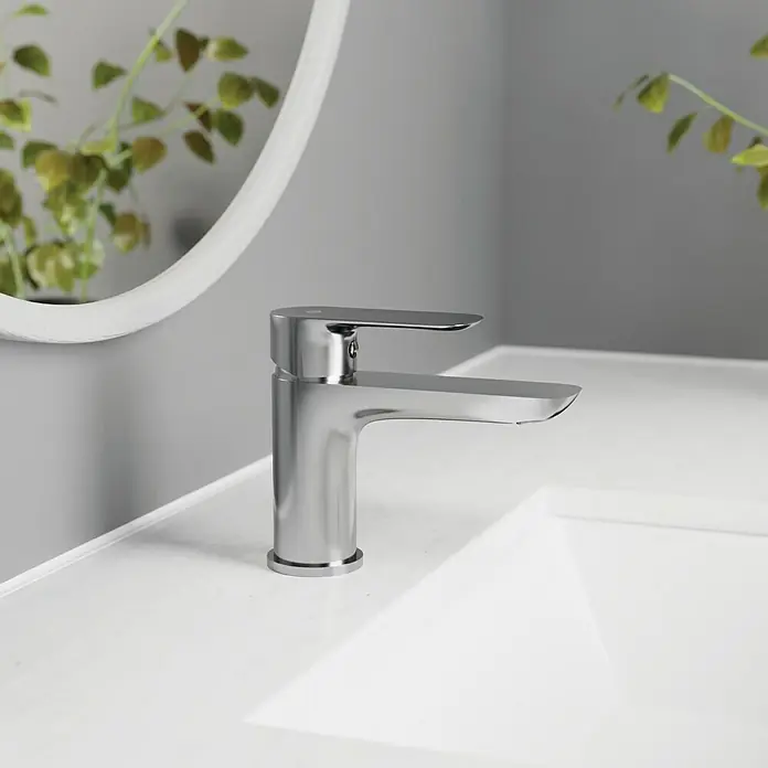 IO Cassio Grifo de lavabo - Cromo - Primer plano de un moderno grifo cromado brillante en un lavabo blanco, con un espejo redondo visible al fondo.