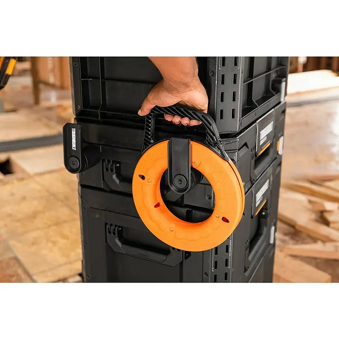 ToughBuilt StackTech Kabelhalter - Kunststoff - Nahaufnahme eines Toughbuilt-Werkzeugkastens mit einer daran befestigten orangefarbenen Kabeltrommel, die von einer Hand gehalten wird.