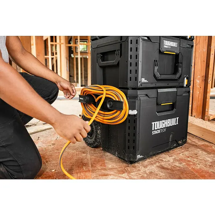 ToughBuilt StackTech Kabelhalter - Kunststoff - Nahaufnahme von zwei schwarzen Toughbuilt Stacktech Werkzeugkisten auf einer Baustelle, eine mit einer gelben Kabeltrommel, die an der Seite befestigt ist.