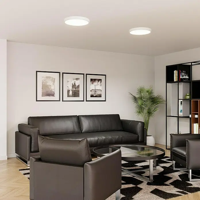 Alverlamp Downlight empotrable LED redondo - 40 W, Ø x Al: 40 x 4 cm, Blanco cálido - Salón moderno con un elegante sofá de cuero, sillones y una mesa de centro elegante sobre una alfombra geométrica. Dos luces de techo iluminan el espacio.