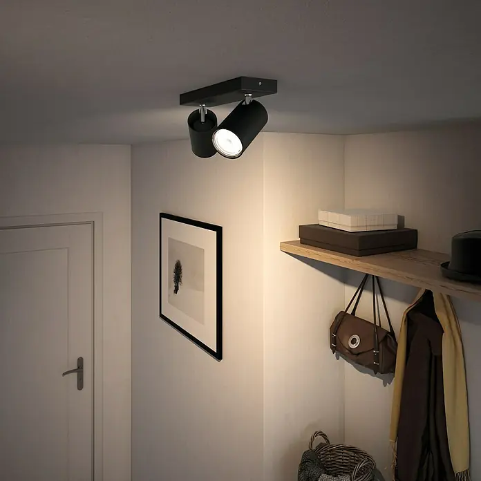 Philips Regleta Kosipo - 10 W, L x An x Al: 9,2 x 24 x 11,8 cm, Negro, GU10, 2 ud. - Disparo de un moderno accesorio de techo de dos luces en un pasillo, con una puerta, un estante y una fotografía enmarcada.
