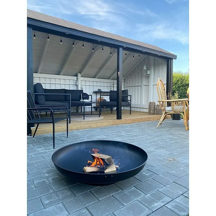 Plus Gartenhaus Multi - Außenmaß inkl. Dachüberstand (B x T): 446 x 266 cm, Holz, Natur, Offen inkl. Halboffen inkl. Dachpappe und Aluleisten - Schwarze Metall-Feuerschale mit brennendem Holz auf Pflaster einer Terrasse.