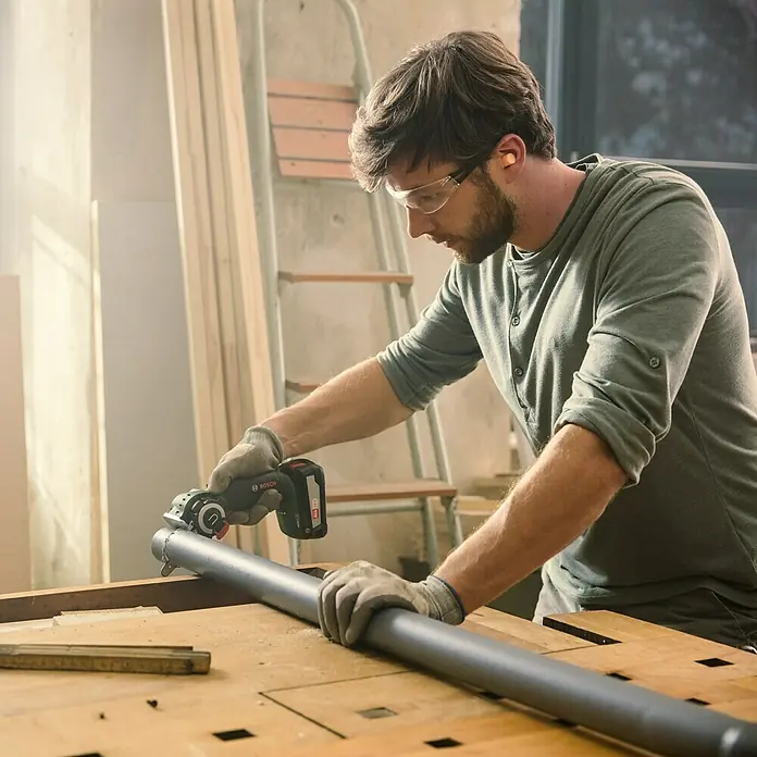 Bosch Power for All 18V NanoBlade-Säge AdvancedCut 18Leerlaufdrehzahl: 7.000 U/min, 18 V, Ohne Akku - Ein Mann, der eine Bosch Akku-Trennsäge benutzt, um ein Rohr zu schneiden, trägt dabei Schutzbrille und Handschuhe.