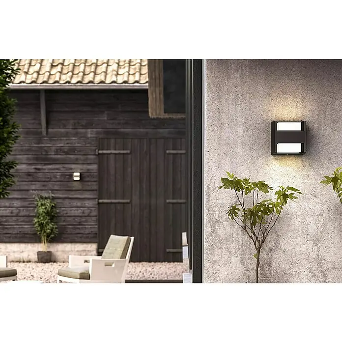 Philips Arbour LED-Außenwandleuchte - 3,8 W, 13 x 13 x 13 cm, IP44 - Nahaufnahme einer modernen, schwarzen Außenleuchte an einer grauen Wand, die ein warmes Licht abstrahlt und die Umgebung stilvoll beleuchtet.