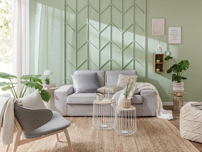 Kleines, helles Wohnzimmer mit grauer Couch und Sessel. Die Wand ist in Mintgrün gestrichen und mit einem DIY Fischgrät-Muster verziert