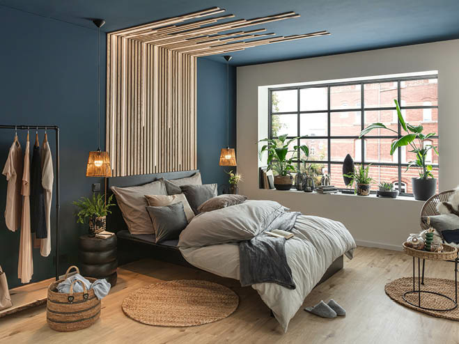 Blick auf Schlafzimmer. Wände sind mit Paneele und dunkelblauer Farbe verziert und am großen Fenstern sind Zimmerpflanzen platziert