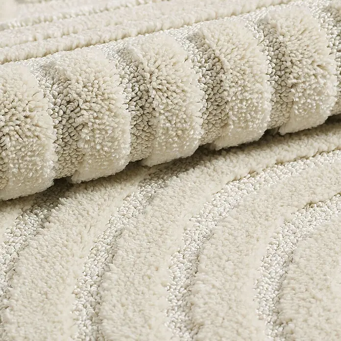 Kurzflorteppich Art - Creme, Durchmesser: 80 cm, 100 % Polypropylen - Nahaufnahme eines gerollten, cremefarbenen Teppichs mit einem erhabenen Streifendesign, das Textur und Komfort betont.