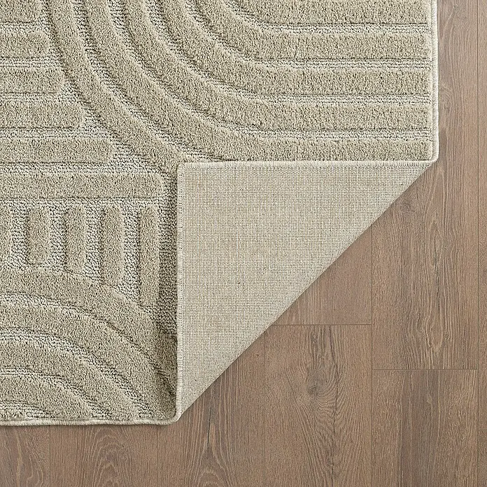 Kurzflorteppich Art - Beige, 150 x 80 cm, 100 % Polypropylen - Detailansicht eines beigefarbenen Teppichs mit modernem Muster und umgeschlagener Ecke, der seine Textur und Unterseite zeigt.