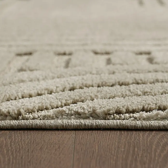 Kurzflorteppich Art - Beige, 150 x 80 cm, 100 % Polypropylen - Nahaufnahme eines beigen Teppichs mit einem dezenten Muster und einer weichen Textur, der auf einem Holzboden liegt.