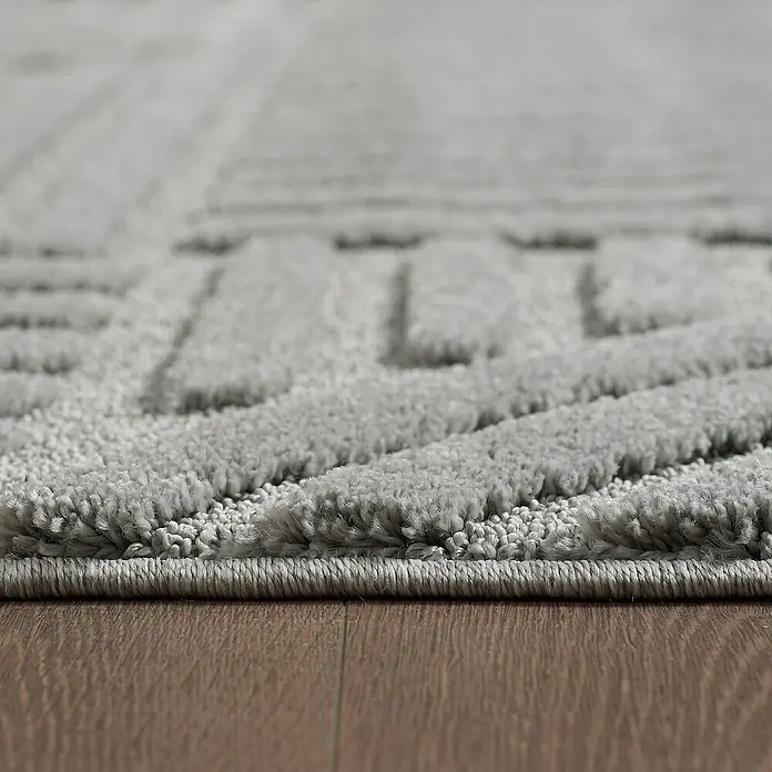 Kurzflorteppich Art - Silber, 290 x 200 cm, 100 % Polypropylen - Nahaufnahme eines grauen Teppichs mit geometrischem Muster, der auf einem Holzboden liegt. Der Teppich hat eine weiche Textur.