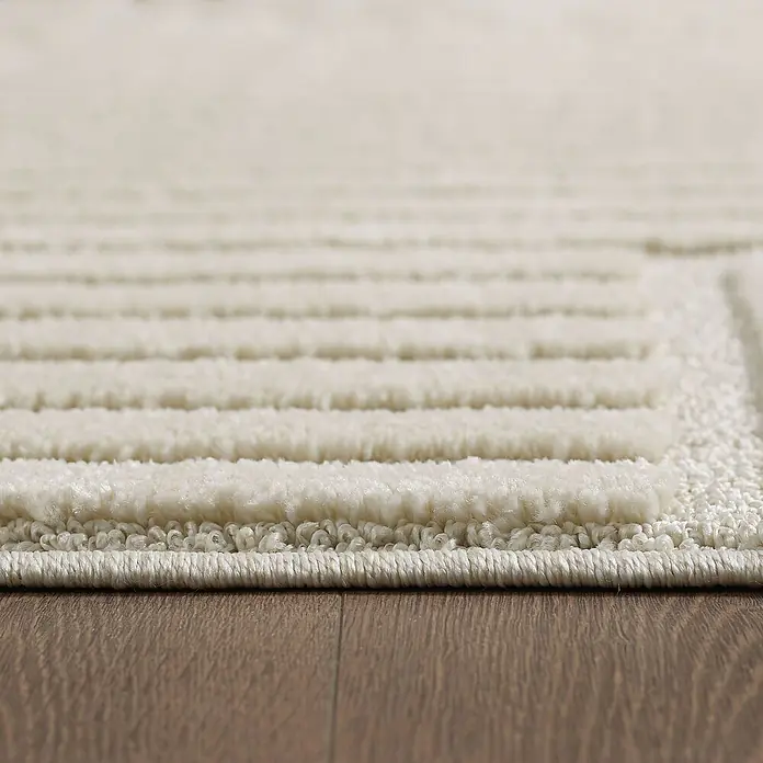 Kurzflorteppich Art - Creme, Durchmesser: 80 cm, 100 % Polypropylen - Nahaufnahme eines stilvollen, elfenbeinfarbenen Teppichs mit erhabenen Streifen, der eine elegante Textur und ein weiches Gefühl vermittelt.
