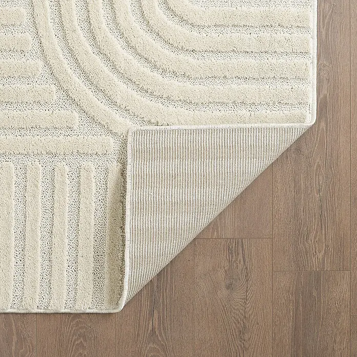 Kurzflorteppich Art - Creme, Durchmesser: 80 cm, 100 % Polypropylen - Nahaufnahme eines beigen Teppichs mit geometrischem Muster auf einem Holzboden, der seine Textur und sein Design hervorhebt.