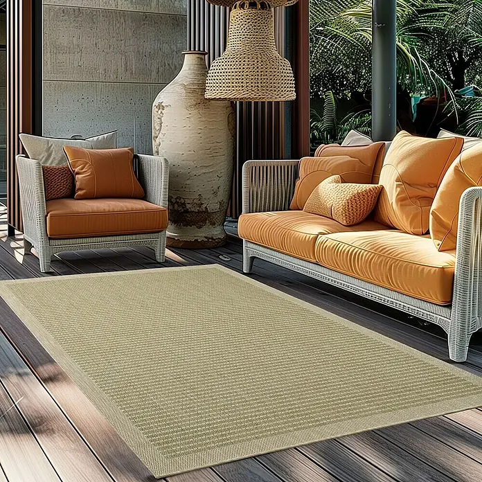 Outdoor-Teppich Giza 1410 - Grün, 170 x 120 cm, 100 % Polypropylen - Ein beigefarbener Teppich liegt auf einer Terrasse, umgeben von Korbmöbeln und üppigem Grün. Der Teppich ist wetterfest und stilvoll.