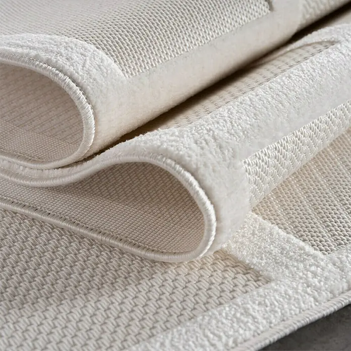 Kurzflorteppich Doha 1657 - Creme, 200 x 140 cm, 100 % Polypropylen - Detailaufnahme eines cremefarbenen Teppichs mit Bordüre, der aufgerollt die Textur und die Verarbeitung hervorhebt.