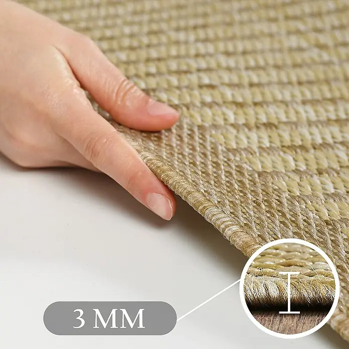Outdoor-Teppich Giza 1410 - Beige, 370 x 280 cm, 100 % Polypropylen - Nahaufnahme einer Hand, die eine Ecke eines beigen gewebten Teppichs hält und dessen 3 mm dünnes Profil und Textur hervorhebt.