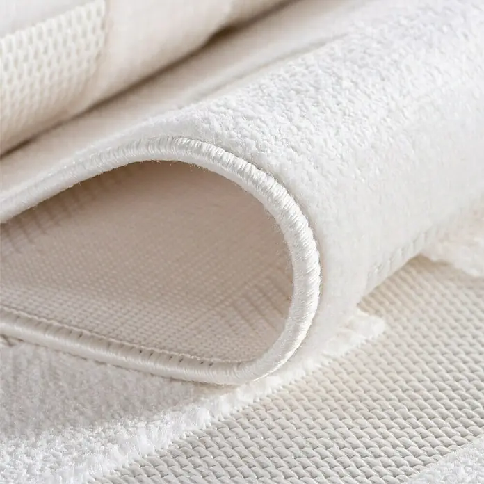 Kurzflorteppich Doha 1656 - Creme, 150 x 80 cm, 100 % Polypropylen - Nahaufnahme einer gerollten, flauschigen, weißen Badematte, die ihre Textur und Verarbeitung zeigt.