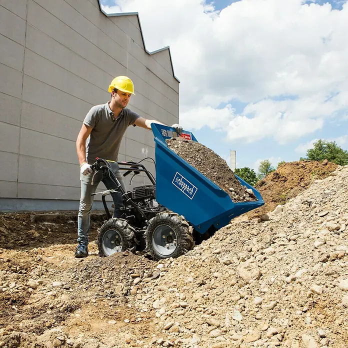 Scheppach Volquete con ruedas DP3000 - 4.100 W, 196 cm³, Capacidad volumétrica: 125 l, Gasolina - Un trabajador de la construcción descarga una carretilla motorizada azul Scheppach llena de grava en una obra.