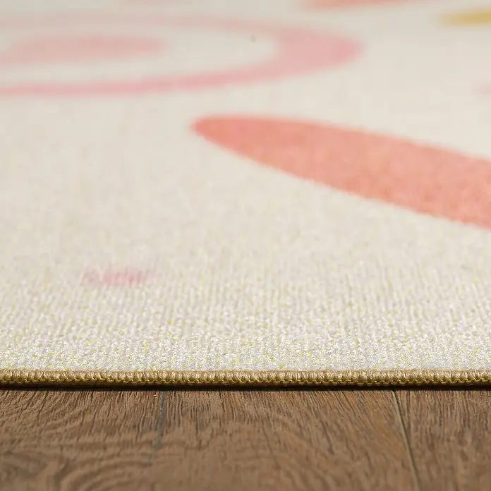 Kinderteppich Play 2021 - Creme, 170 x 120 cm, 100 % Polypropylen - Nahaufnahme eines Teppichs mit rosa Kreismuster und braunem Holzboden.