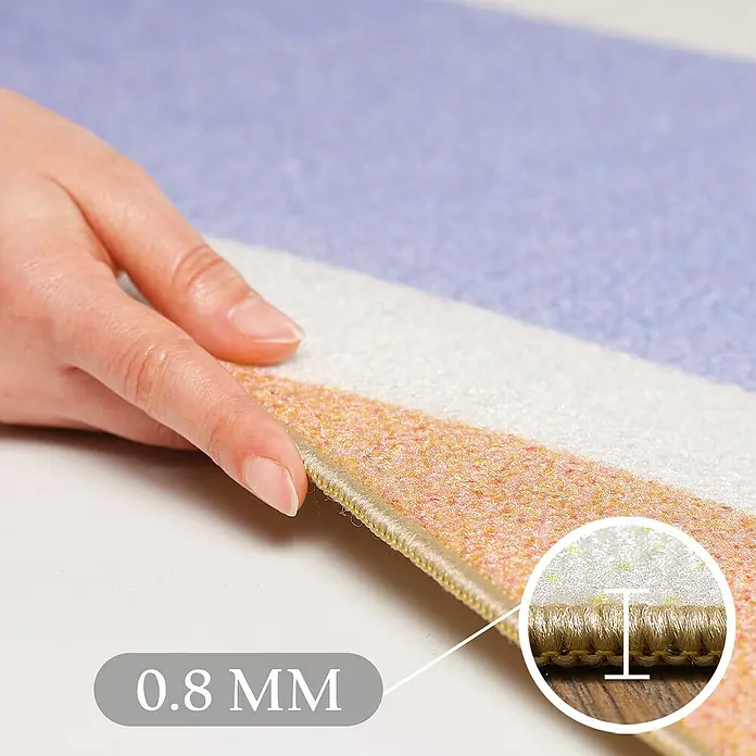 Kinderteppich Play 2020 - Bunt, 150 x 100 cm, 100 % Polypropylen - Nahaufnahme einer Hand, die einen mehrfarbigen, strukturierten Teppich mit 0,8 mm Dicke berührt und sein niedriges Profil hervorhebt.