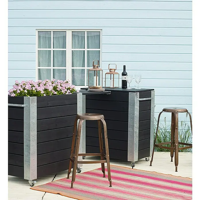Plus Pflanzkasten Cubic - Außenmaß (L x B x H): 87 x 50 x 95 cm, Holz, Schwarz/Silber - Dunkelholz-Mobilbar- und Pflanzkübel-Set mit Metallakzenten und Barhockern, auf Terrasse mit pinken Blumen.
