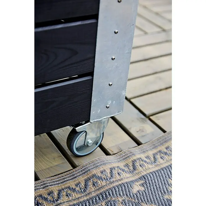 Plus Pflanzkasten Cubic - Außenmaß (L x B x H): 120 x 50 x 95 cm, Holz, Schwarz/Silber - Dunkle Holzpflanzkiste mit Metallecke und Lenkrolle auf Holzterrasse neben gemustertem Teppich.