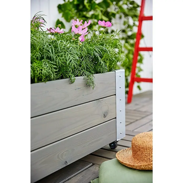 Plus Pflanzkasten Cubic - Außenmaß (L x B x H): 120 x 50 x 45 cm, Holz, Grau/Braun - Graues Holz-Pflanzgefäß mit Metallakzenten, gefüllt mit rosa Kosmeen, auf Rollen auf einer Terrasse.