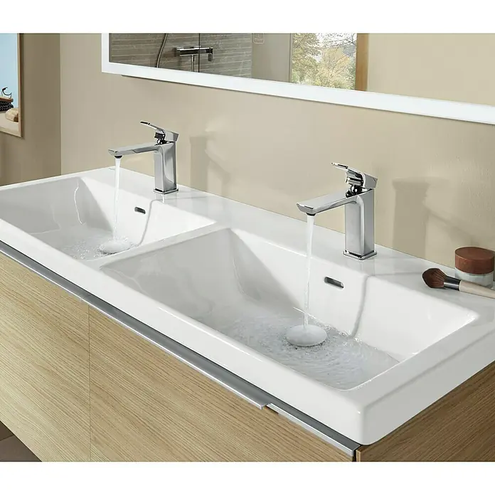 Villeroy & Boch Subway 3.0 Aufsatzwaschbecken - Mit schmutzabweisender Glasur, Mit Überlauf, Stone White, Anzahl Hahnlöcher: 2, Anzahl Waschschüsseln: 2 Stk. - Doppelter weißer Keramik-Waschtisch mit zwei Chromarmaturen, aus denen Wasser läuft, auf einem hellen Holzschrank.