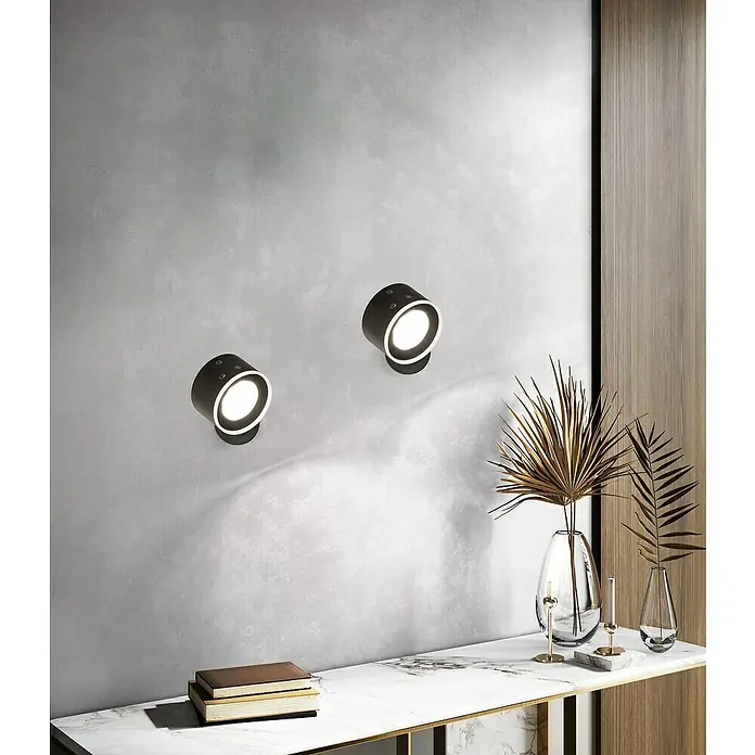 FHL easy Magnetic Akku-Wandleuchte - 8 x 8 x 5 cm, Schwarz, Warmweiß, 1,5 W, IP20 - Zwei schwarze zylindrische Wandleuchten mit weißen Innenringen beleuchten eine strukturierte Wand über einer Marmorkonsole.