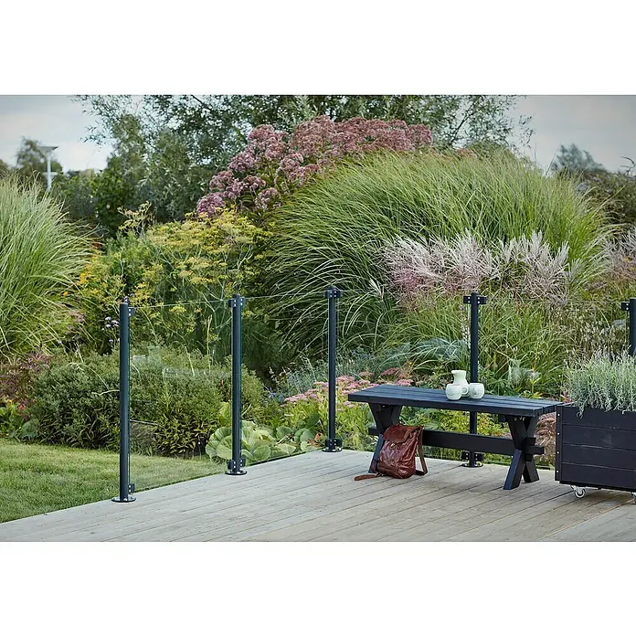 Plus Zaunpfosten mit Fuß und Schrauben - Höhe: 96 cm, Durchmesser: 4,24 cm, Grauschwarz, Stahl - Der schlichte, dunkle Gartentisch mit Bank und Dekoration steht auf einer Holzterrasse, umgeben von üppiger Gartengestaltung.