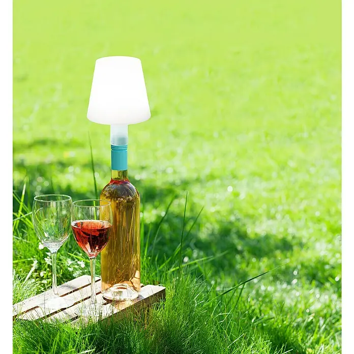 FHL easy Akku-Tischleuchte Flaschenleuchte Fiocco - 1,5 W, Ø x H: 12 x 11 cm, Weiß, RGBW - Weiße tragbare Lampe mit türkisfarbenem Sockel, auf einer Roséweinflasche angebracht, daneben zwei Weingläser.